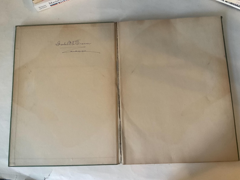 Op de afbeelding: Open boek met verouderde, cr&egrave;mekleurige pagina's. De linkerpagina heeft een handgeschreven handtekening boven een datum. De randen van het boek zijn donkergroen. De pagina's vertonen tekenen van ouderdom en gebruik.