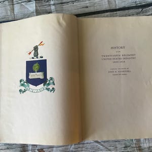May include: Open book with the title page of a military history book. The left page features a crest with a palm tree and the word "ONWARD". The right page displays the title "HISTORY of the TWENTY-FIFTH REGIMENT UNITED STATES INFANTRY 1869-1926".
