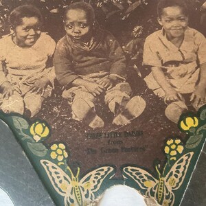 Op de afbeelding: Sepia-getinte afbeelding van drie kinderen die op gras zitten. De afbeelding is omlijst door een decoratieve rand met vlinders en bloemmotieven. De tekst luidt "Three Little Babies from The Green Pastures."