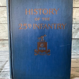 May include: A vintage book titled "History of the 25th Infantry" with gold lettering on a blue cover. The cover also features a gold emblem. The book is closed and appears to be in good condition.