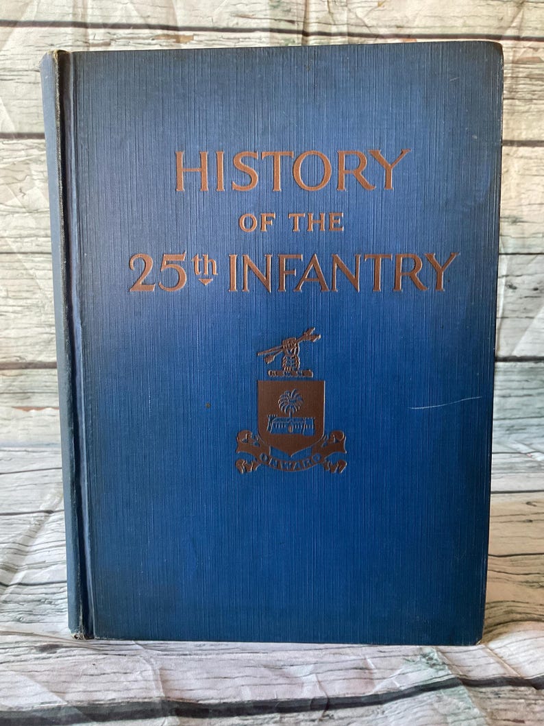 May include: A vintage book titled "History of the 25th Infantry" with gold lettering on a blue cover. The cover also features a gold emblem. The book is closed and appears to be in good condition.