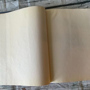 May include: An open book with aged, cream-colored pages. The book's spine is dark blue, and the pages are slightly yellowed, suggesting age. The book is lying open on a weathered, light-colored wooden surface.