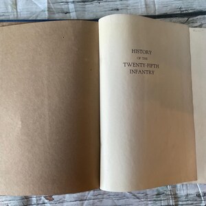 May include: Open book with a blue cover and aged pages. The text "HISTORY OF THE TWENTY-FIFTH INFANTRY" is printed in black on the right page. The left page is blank.