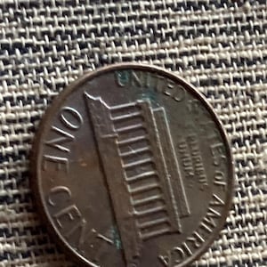 Puede incluir: Una moneda estadounidense de un centavo de color cobre. La moneda presenta las palabras "ONE CENT" y "UNITED STATES OF AMERICA". La imagen muestra el Lincoln Memorial en el reverso de la moneda.