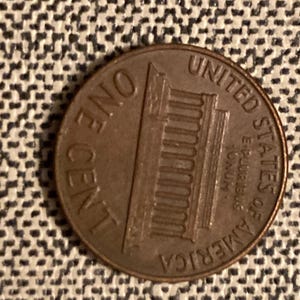 Puede incluir: Una moneda de un centavo estadounidense de color cobre con el Lincoln Memorial y las palabras "ONE CENT" y "UNITED STATES OF AMERICA" en ella.