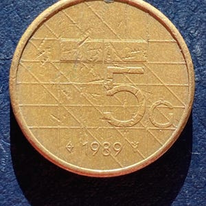 May include: A close-up of a bronze coin with the number 5 and the year 1989. The coin has a grid-like pattern across its surface and a raised edge. The coin is circular and has a golden hue.