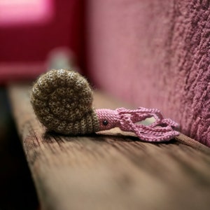 May include: A crocheted amigurumi toy shaped like a nautilus with a pink body and brown shell.
