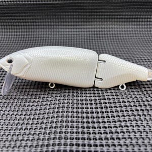 May include: A two-piece, articulated fishing lure in a pearlescent white finish. The lure features a clear plastic lip, two eyelets, and a textured scale pattern. The lure is designed to mimic a small fish.