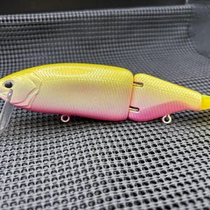 May include: A two-piece fishing lure with a yellow and pink gradient body, a clear plastic lip, and a yellow tail. The lure has two metal eyelets and a hook attachment point. The lure is designed to mimic a small fish.