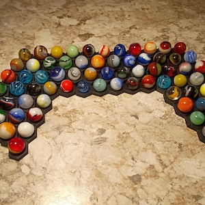 May include: A collection of colorful marbles arranged on a black honeycomb-shaped base. The marbles are various sizes and colors, including red, blue, green, yellow, and orange. The base is approximately 12 inches wide.