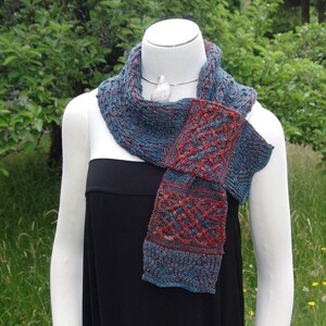 May include: A blue and red knitted scarf with a Celtic knot pattern. The scarf is draped around a mannequin's neck.