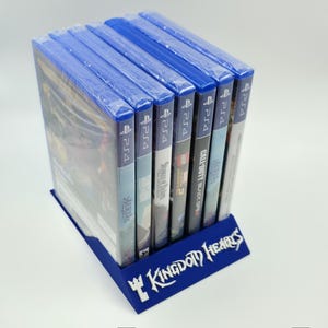 May include: A blue plastic display stand holding several PS4 video game cases. The stand has the words "Kingdom Hearts" in white lettering. The game cases are in plastic wrap.