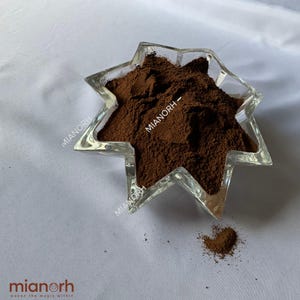 May include: A star-shaped clear glass bowl filled with a fine, dark brown powder. The text MIANORH is printed on the glass and appears multiple times across the surface of the bowl. A small amount of the brown powder is scattered outside the bowl.