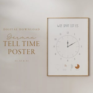 May include: A printable poster with a clock face and the text "Wie spät ist es?" in German. The clock face has a gray background with black hands and black numbers. The poster is framed in a gold frame and is hanging on a white wall.