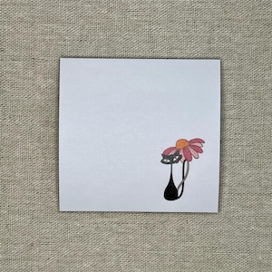 Op de afbeelding: Een zwarte kat met een roze en oranje bloem op zijn kop. De kat kijkt naar rechts.