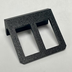 May include: Black plastic double toggle switch plate with a textured surface.