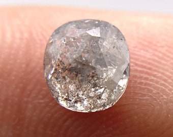 May include: A round, clear, faceted diamond with a gray tint. The diamond is about 5mm in diameter and has a rough, unpolished surface.