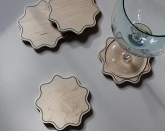 May include: Four light-colored wooden coasters with a wavy, scalloped edge and a thin, dark-colored border line. One coaster supports a clear glass goblet. The coasters have a smooth, natural wood grain finish and a distinct, repetitive star-like shape.