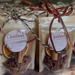 May include: Clear plastic pouches containing dried orange slices, cinnamon sticks, and spices for a stovetop potpourri simmer. Each pouch features a round white label with the text Christmas Stovetop Potpourri Simmer and is tied with a red and green ribbon.