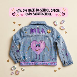 May include: A light blue denim jacket featuring the name MIA in purple letters, a central purple heart character with arms and legs, and scattered colorful stars and hearts. The text 10% OFF BACK-TO-SCHOOL SPECIAL Code: BACKTOSCHOOL appears above.
