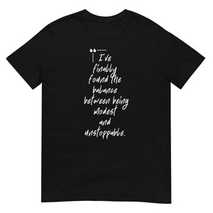 May include: Black t-shirt with white text that reads "I've finally found the balance between being modest and unstoppable."