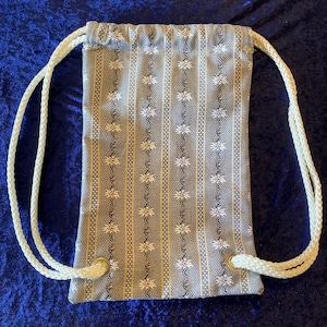 May include: A gray and white drawstring bag with a floral pattern. The bag has white drawstrings and brass grommets.