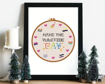 Könnte beinhalten: Ein gerahmter Stickrahmen mit weißem Hintergrund und bunter Stickerei, die eine Regenbogenflagge, Herzen und den Text "Make the Yuletide Gay!" zeigt.