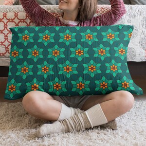 May include: A person is sitting on a white rug with a green and orange patterned pillow in their lap. The pillow has a geometric design with star-shaped patterns.