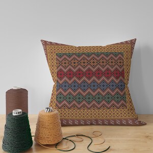 May include: A brown throw pillow with a geometric pattern in shades of red, blue, green, and yellow. The pillow has a brown border with a gold and white geometric pattern.