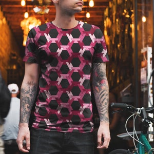 May include: A man wearing a black and pink geometric patterned t-shirt. The shirt has a hexagonal pattern with pink and red shades.