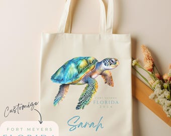 May include: A cream-colored canvas tote bag featuring a colorful watercolor sea turtle illustration. Below the turtle, the text reads Fort Meyers Florida 2024 and the name Sarah in blue script. A separate label shows the text Customize Fort Meyers Florida 2024.