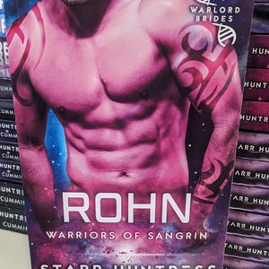 May include: A paperback book cover with a muscular man on the front. The cover is pink and purple with a galaxy background. The title of the book is "ROHN: WARRIORS OF SANGRIN" by Starr Huntress and Nancy Cummings.