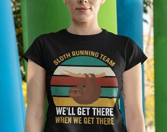 Puede incluir: Camiseta negra con un gráfico de estilo retro de un perezoso colgado de una rama. El gráfico dice "Sloth Running Team" y "We'll Get There When We Get There".
