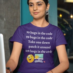 Op de afbeelding: Een paars t-shirt met de tekst "99 bugs in the code" en een knipoog-emoji met een computerafbeelding. Het shirt wordt gedragen door een persoon die aan een bureau met een laptop zit.