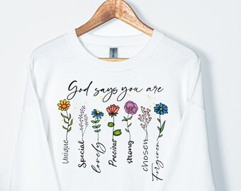 Könnte beinhalten: Weißer Pullover mit einem Blumenmuster und dem Text "God says you are" mit den Wörtern "einzigartig, besonders, liebenswert, kostbar, stark, auserwählt, vergeben" vertikal neben jeder Blume.