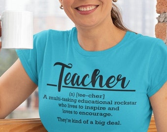 Może przedstawiać: Turkusowy t-shirt z napisem "Teacher" w czarnym kolorze. Na koszulce znajduje się definicja słowa "Teacher". Definicja brzmi: "(n) [tee-cher] Multitaskingowa gwiazda rocka edukacji, która żyje, aby inspirować i kocha zachęcać. Są wielką sprawą."