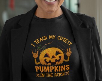 Könnte beinhalten: Ein schwarzes T-Shirt mit einer Grafik eines lächelnden Kürbisses, dessen Arme Handgesten machen. Der Text lautet I TEACH MY CUTEST PUMPKINS IN THE PATCH. Das T-Shirt wird unter einem schwarzen Blazer getragen, was einen professionellen Look ergibt.