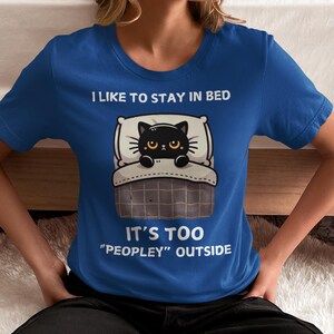 May include: A blue t-shirt with a black cat in bed and the text "I like to stay in bed. It's too "peopley" outside."