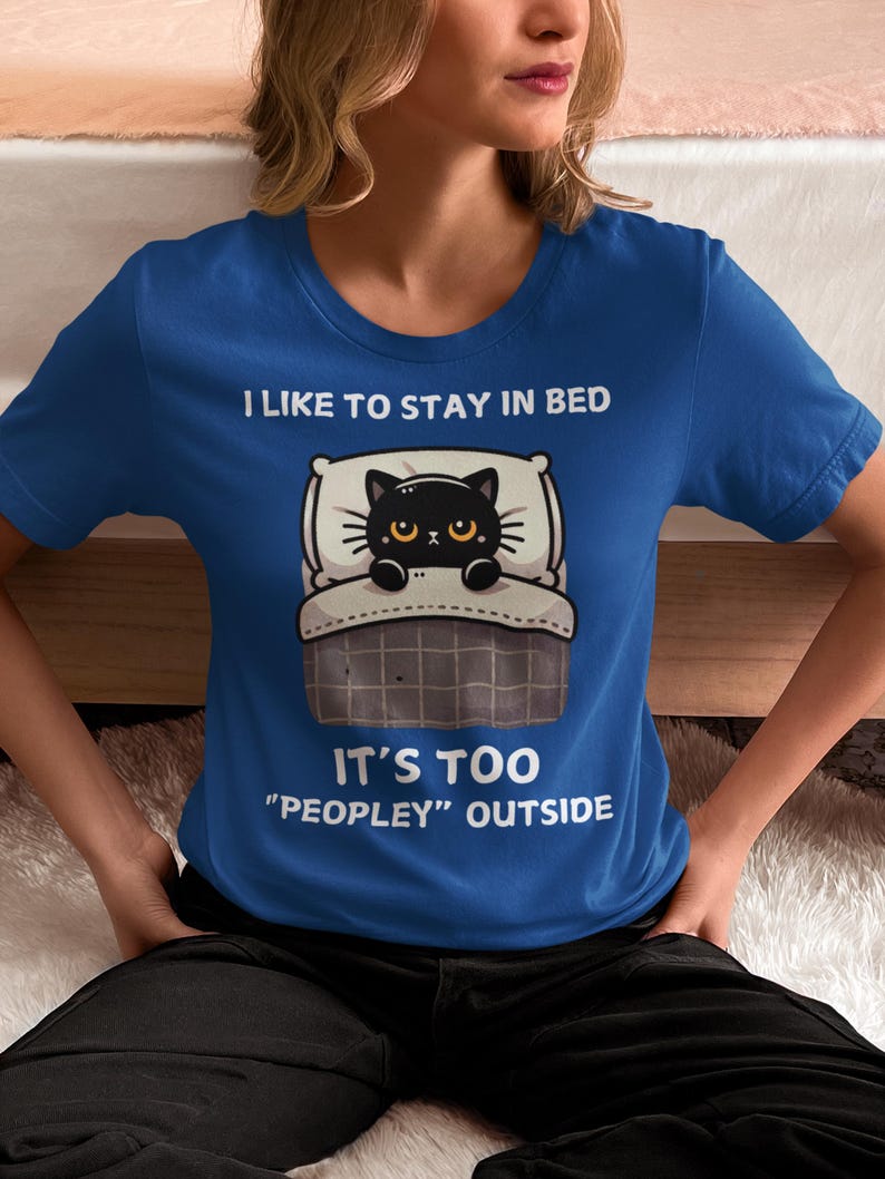 May include: A blue t-shirt with a black cat in bed and the text "I like to stay in bed. It's too "peopley" outside."