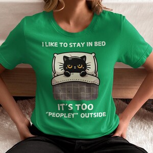 May include: A green t-shirt with a black cat in bed and the text "I like to stay in bed. It's too "peopley" outside."