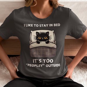 May include: A dark gray t-shirt with a black cat in bed and the text "I like to stay in bed. It's too "peopley" outside."