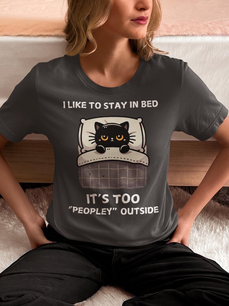 May include: A dark gray t-shirt with a black cat in bed and the text "I like to stay in bed. It's too "peopley" outside."