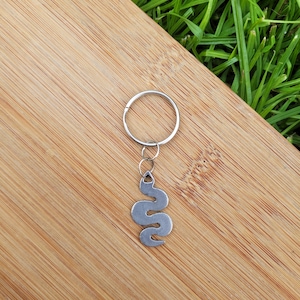 May include: Silver snake keyring with a silver key ring. The keyring is on a wooden surface.