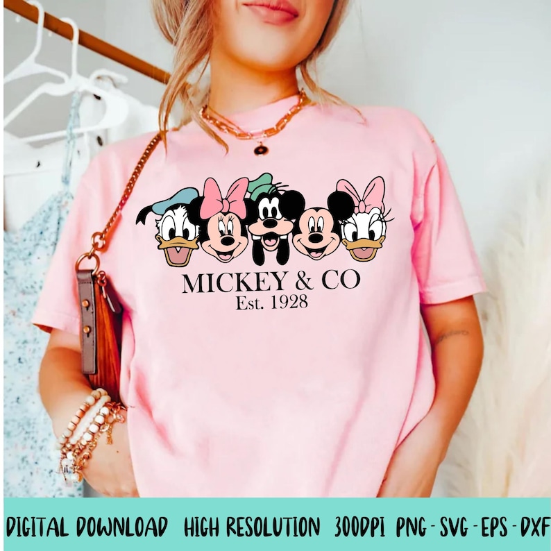 Puede incluir: Camiseta rosa con un gr&aacute;fico de Mickey Mouse, Minnie Mouse, Donald Duck, Goofy y Pluto. El texto "MICKEY & CO Est. 1928" est&aacute; impreso debajo del gr&aacute;fico.