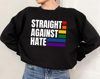 May include: Black sweatshirt with the text "STRAIGHT AGAINST HATE" in white letters. The text is overlaid with a rainbow stripe.