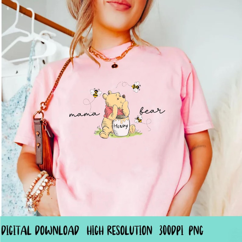 May include: Pink t-shirt featuring a cartoon illustration of Winnie the Pooh with the words "mama bear". The bear is holding a honey pot with the word "Hunny" on it, surrounded by bees. The text "DIGITAL DOWNLOAD HIGH RESOLUTION 300DPI PNG" is at the bottom.