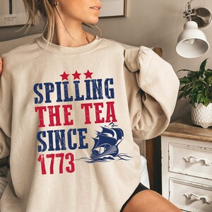 May include: A beige sweatshirt with a blue and red graphic print that says "Spilling the Tea Since 1773" with a ship illustration.