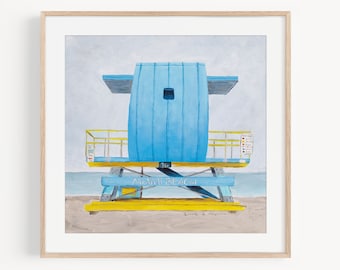 May include: A painting of a blue lifeguard stand on a beach with the words "Miami Beach" written on the front. The stand has a yellow roof and yellow railings. The painting is framed in a light wood frame.