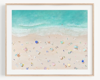May include: An aerial view of a beach with turquoise water and white sand.  People are scattered across the beach, enjoying the sun and relaxing under colorful umbrellas.