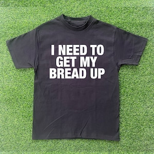 Op de afbeelding: Zwart T-shirt met witte tekst die "Ik moet mijn brood verdienen." zegt.